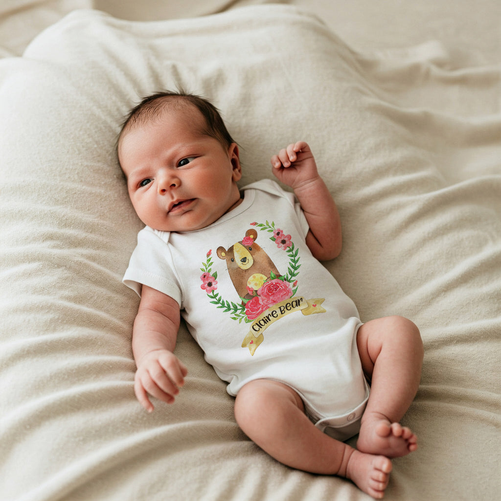 Baby wearing a white onesie with a bear design on a beige blanket