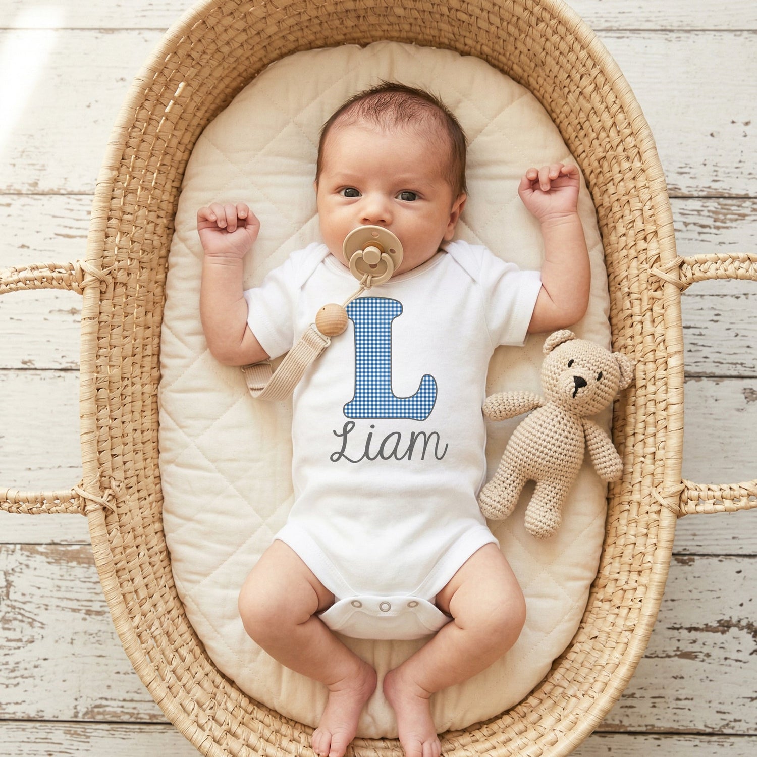 Baby in a crib with a pacifier and teddy bear, wearing a onesie with 'Liam' on it.