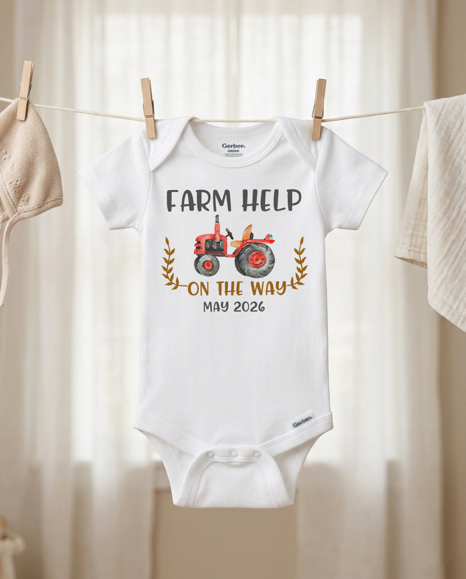 Baby onesie with 'Farm Help on the Way May 2026' text and tractor graphic hanging on a line.