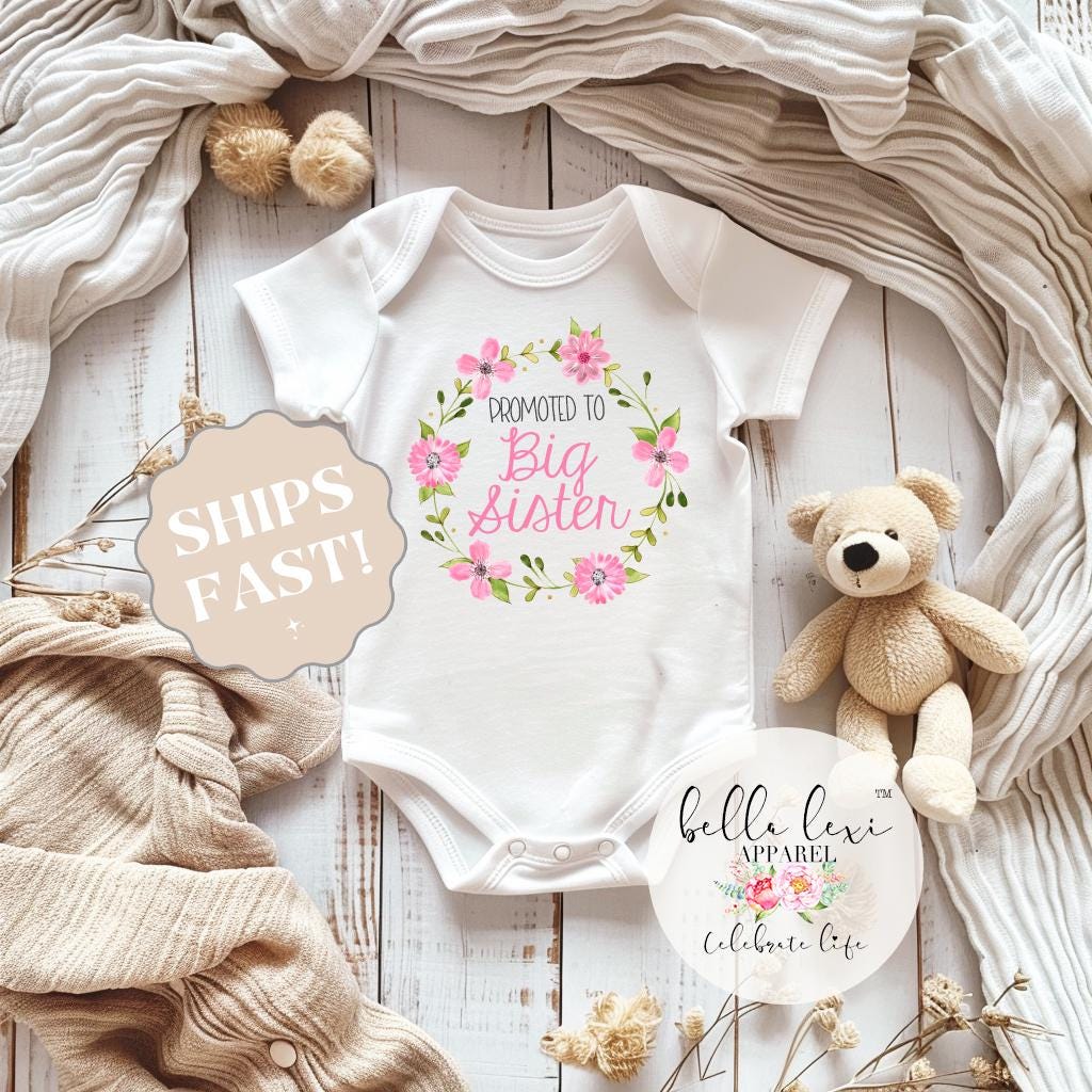 May include: White baby onesie with pink floral wreath and the text "Promoted to Big Sister".