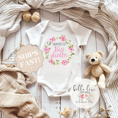 May include: White baby onesie with pink floral wreath and the text "Promoted to Big Sister".