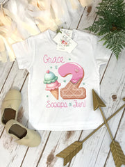 May include: White t-shirt with a pink and white ice cream cone and a pink donut with a pink heart on top. The text "Grace is 2 Scoops of Fun!" is printed on the shirt.
