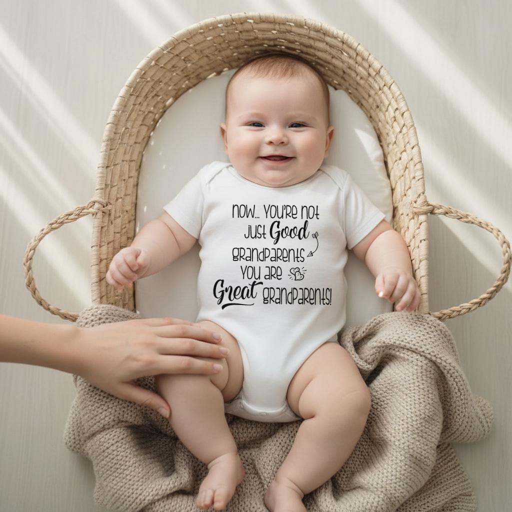 May include: A white short-sleeved baby bodysuit featuring black text that reads: Now... YOU'RE NOT JUST Good GRANDPARENTS YOU ARE Great GRANDPARENTS! The garment is made of a soft fabric and is designed with a simple crew neckline and snap closures.