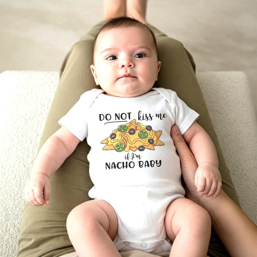 May include: A white short-sleeved baby bodysuit featuring a graphic of yellow nachos with green jalapeño slices and black olives. The text reads DO NOT kiss me if I'm NACHO BABY in black lettering centered on the chest of the garment.