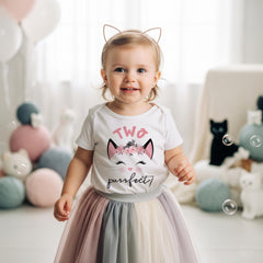 May include: A white short-sleeved bodysuit featuring a graphic of a cat face with a floral crown, the text "TWO" in pink, and the text "purrfect!" in black. The bodysuit is paired with a multi-colored tulle skirt and a cat ear headband.
