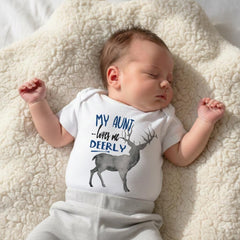 May include: A white short-sleeved baby bodysuit featuring a graphic of a grey deer and the blue text "MY AUNT loves me DEERLY" printed on the front. The garment has a round neckline and is worn by a sleeping infant with light skin and brown hair.