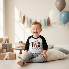 May include: A white and black raglan long-sleeve shirt with the text Two Wild, featuring a red and black buffalo plaid beanie, a black beard, and two crossed axes. The shirt is paired with gray pants, creating a lumberjack-themed birthday outfit.