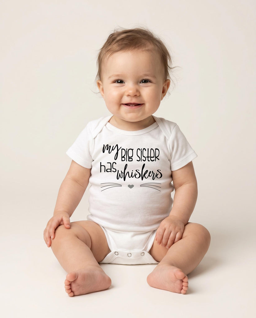 May include: A white short-sleeved baby bodysuit featuring the black printed text "my BIG SISTER has whiskers" with a small heart and thin horizontal lines resembling cat whiskers underneath the lettering on the front of the garment.