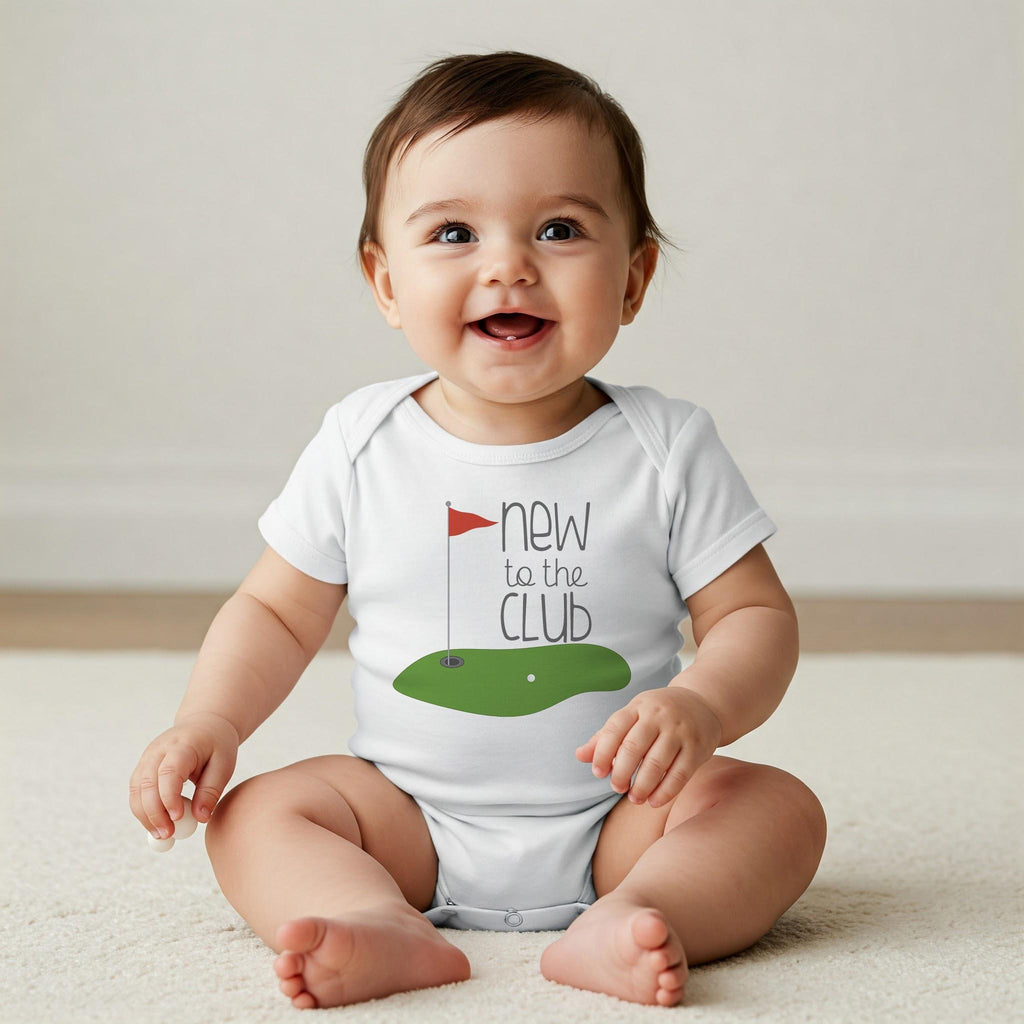May include: A white short-sleeved baby bodysuit featuring a graphic of a green golf putting area with a red flag and the text "new to the CLUB" in dark gray lettering. The design is centered on the chest of the garment.
