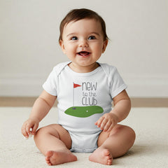 May include: A white short-sleeved baby bodysuit featuring a graphic of a green golf putting area with a red flag and the text "new to the CLUB" in dark gray lettering. The design is centered on the chest of the garment.