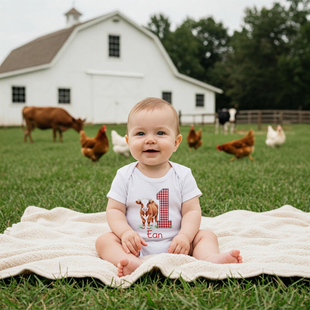 May include: A white short-sleeved baby bodysuit featuring a graphic of a brown calf standing next to a large red and white checkered number one. The name Ean is printed in red cursive script below the calf on the front of the garment.
