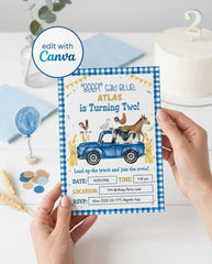 Hands holding a printed 5x7 farm second birthday invitation with a blue gingham border, watercolor blue truck full of farm animals, and "Load up the truck and join the crew" party details, styled on a table with a white cake with a number 2 topper, a blue balloon, confetti, and wheat stalks, with an edit with Canva badge.