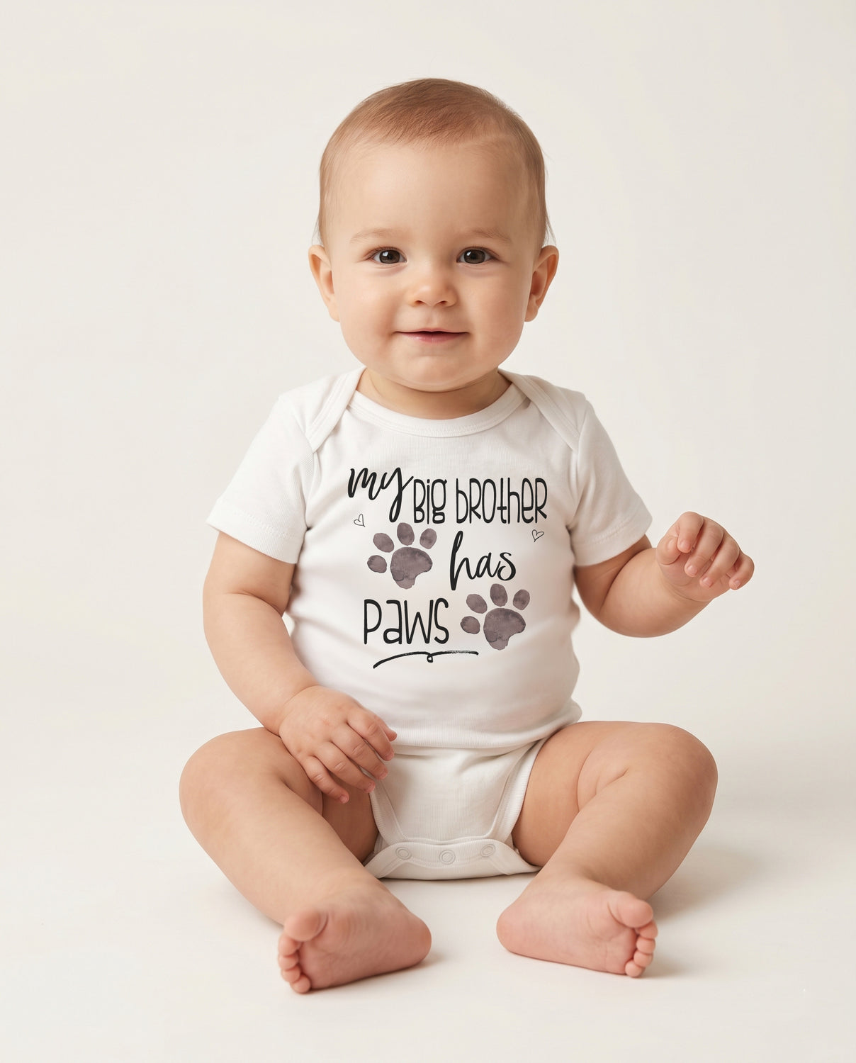 Baby wearing a onesie with 'my big brother has paws' text and paw prints on a white background