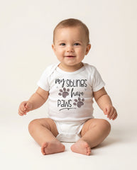 Baby wearing a white onesie with text and paw prints on a light background
