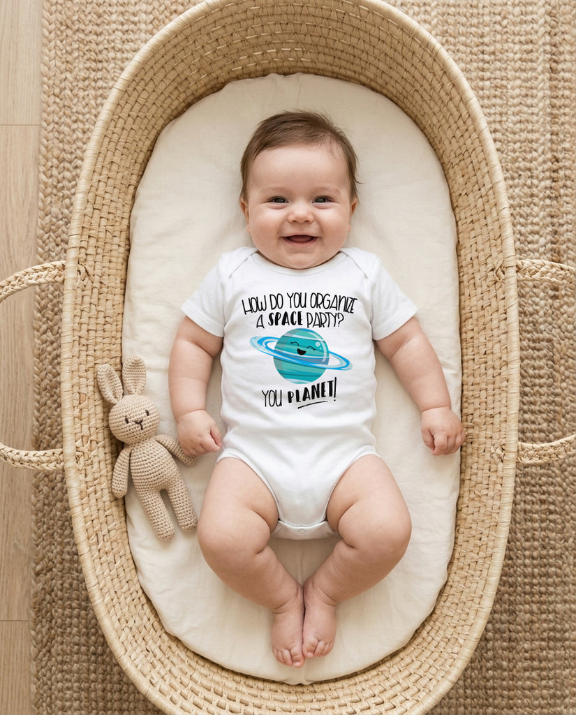 Baby in a Moses basket wearing a onesie with a space-themed design.