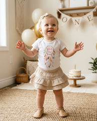 Child wearing a 'Wild One' shirt in a home setting with balloons and a cake.